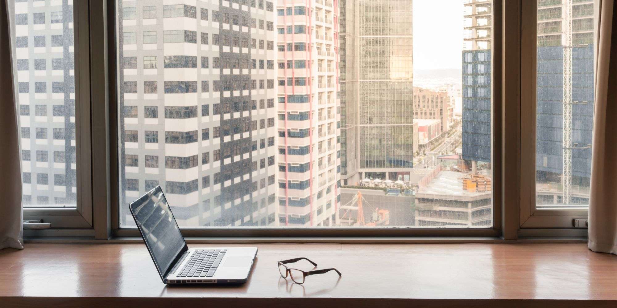 Laptop and glasses on a wooden desk with a city skyline view, illustrating a workspace for change management insights.