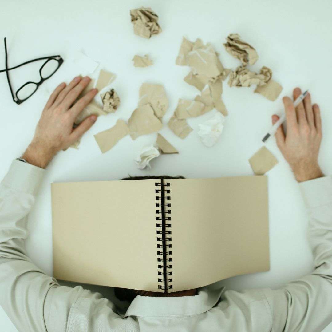 Person with a notebook over their head surrounded by crumpled paper, illustrating change fatigue and stress in organizations.