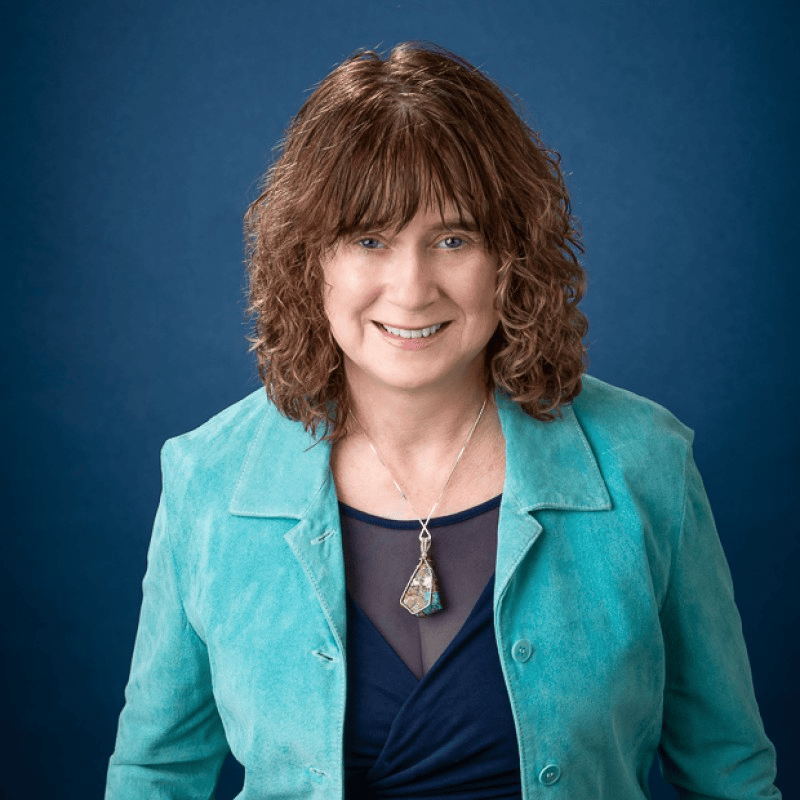 Woman smiling in a turquoise jacket against a navy background, representing expertise in implementation management.