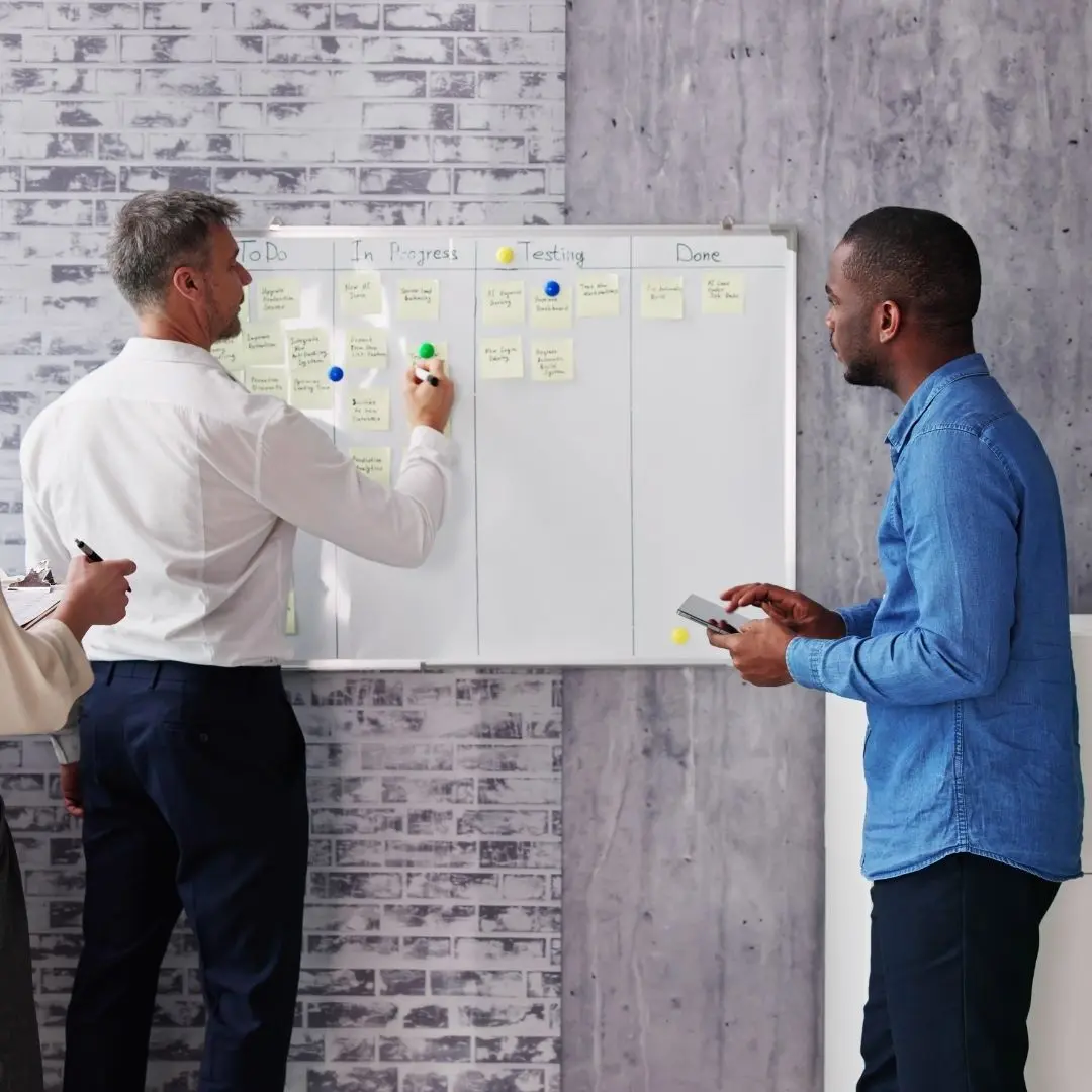 Team collaborating on project management board with sticky notes in office setting.